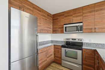 A kitchen with a stainless steel refrigerator, microwave, oven, and wooden cabinets.